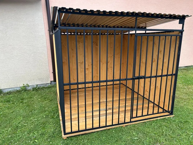 Kojec z drewnianą ścianą tylną i boczną oraz drewnianą podłogą, przy domu